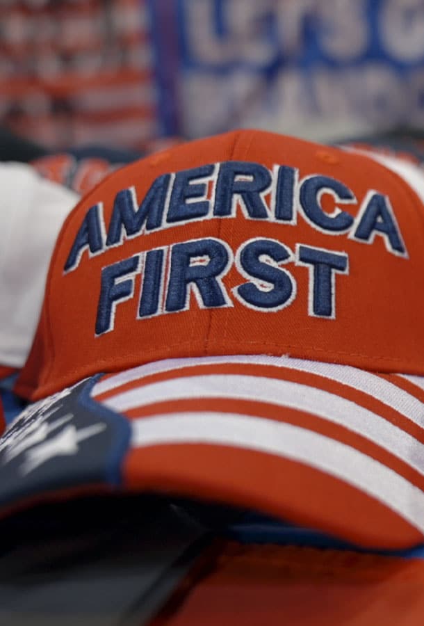 Red hat with stars and stripes on the rim with the words "America First" written in blue bold letters on the hat.