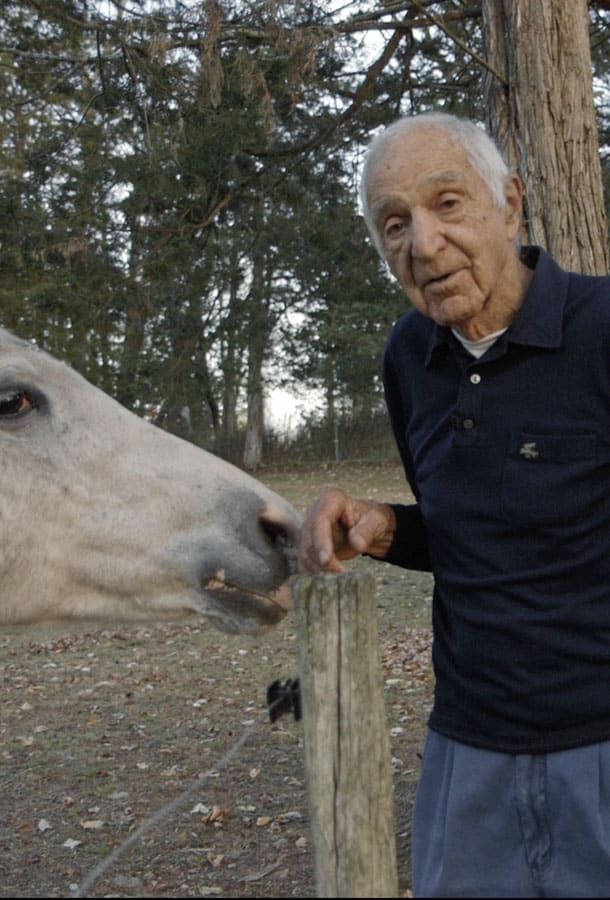 Picture shows an elderly man taking a picture with a horse / donkey