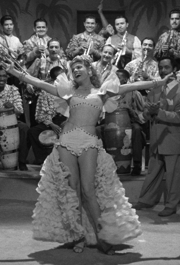 Woman in a dress dancing with arms outstretched in front of band.